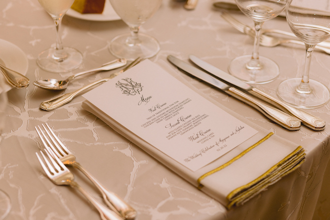 A menu on a white and gold napkin. The menu has the couple's monogram and three courses. 