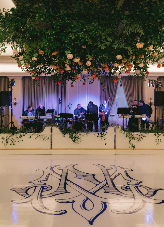 A monogrammed dance floor in front of the band with a canopy of flowers and greenery above it. 