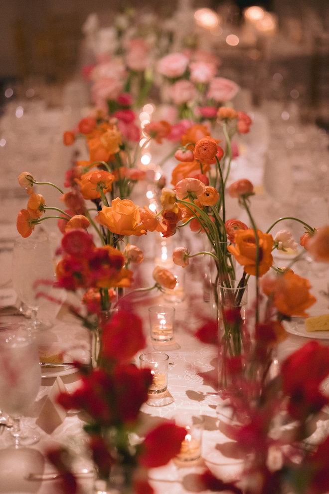 Single stems of red orange and pink flowers in vases lining the reception table. 