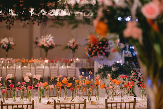 The reception tables decorated with orange and pink flowers and large floral-filled centerpieces.