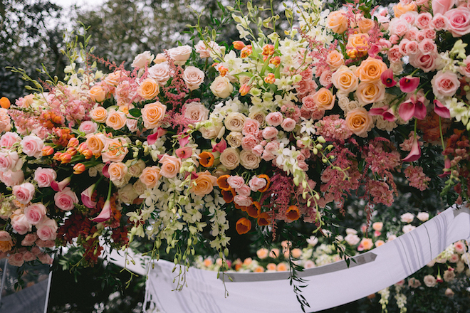 Florals in shades of pink and orange decorating the top of the chuppah. 