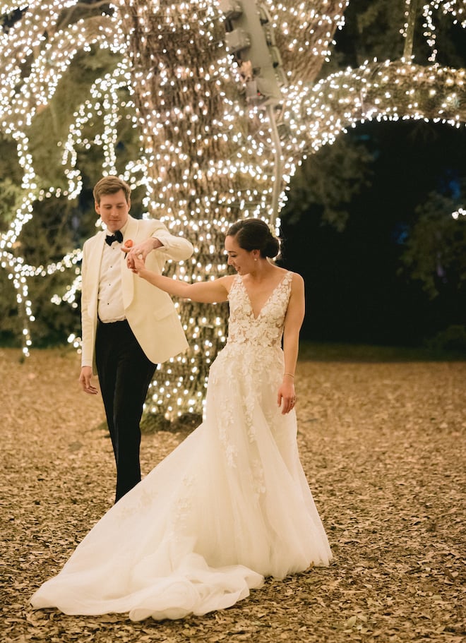 The bride and groom dancing under the lit-up tree. 