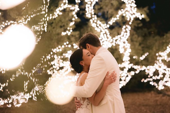 The bride and groom hugging underneath the lit-up tree. 