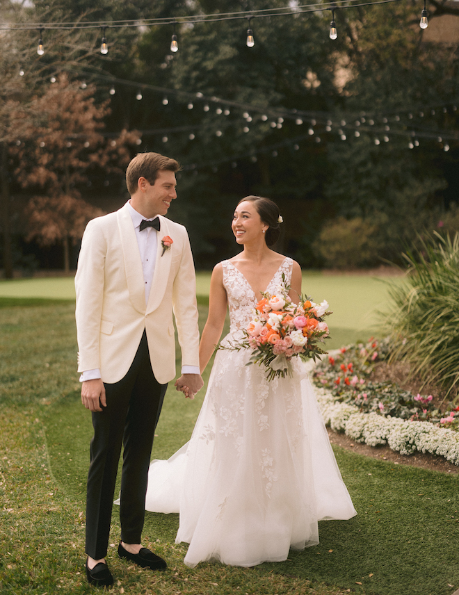 A bride and groom holding hands walking through a lawn.