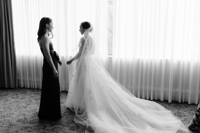 The bride wearing her wedding gown and veil talking to a bridesmaid in a black gown.