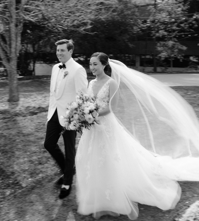 The bride and groom walking with the brides veil flowing behind her. 