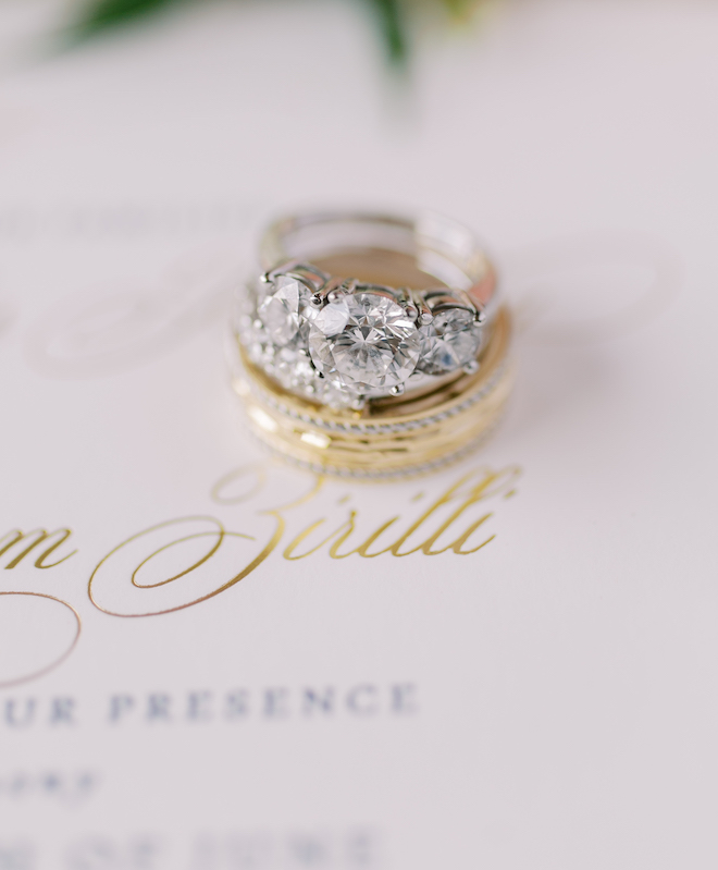 A diamond ring stacked on a gold wedding band sitting on the wedding invitation.