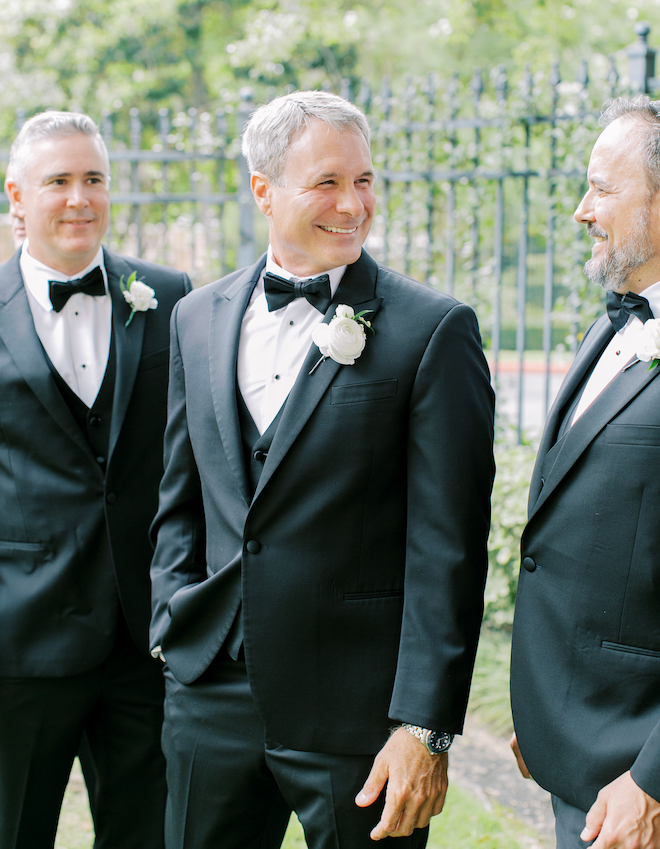 The groom smiling and standing with two groomsmen. 