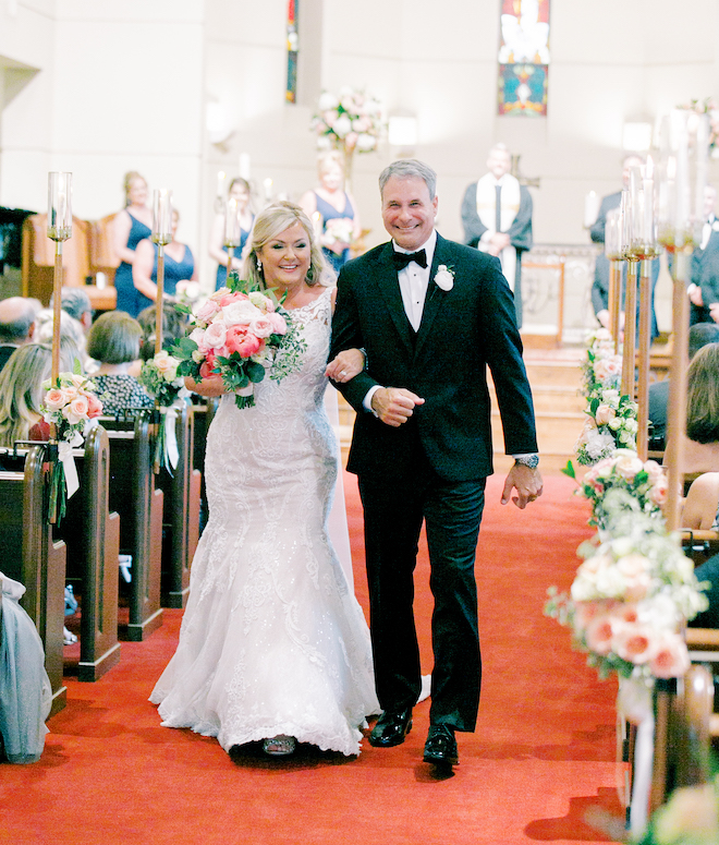 The bride and groom linking arms and smiling walking back down the aisle in the church.