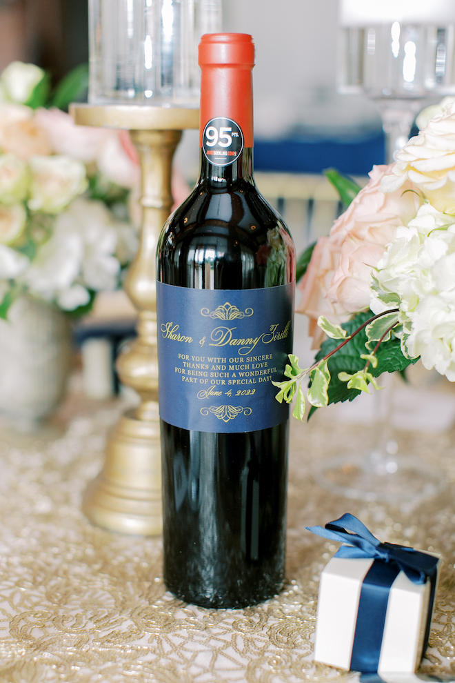 A wine bottle with a custom blue label and gold writing with the couple's name and wedding date. 