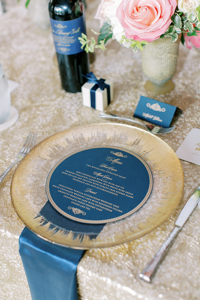 A gold plate with a blue menu with gold writing laying on it. 