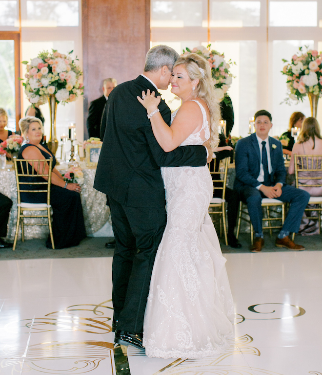 The bride and groom dancing on a white dance floor with a gold monogram. 