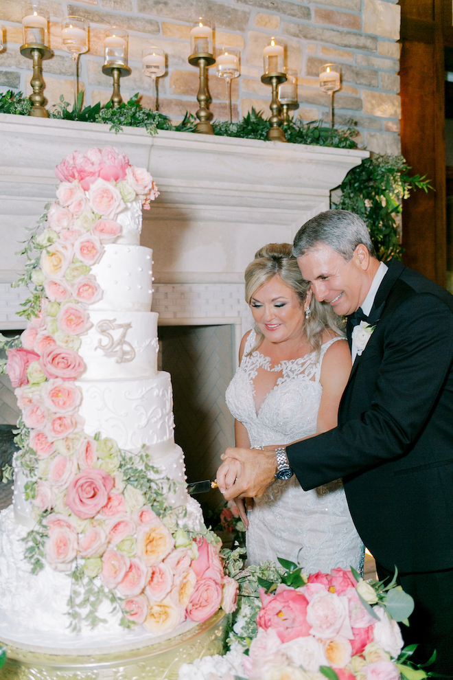 A six tier white wedding cake with their monogram and pink florals going up the cake. 