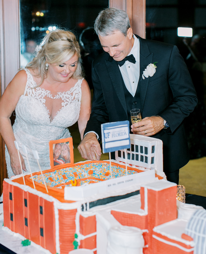 The bride and groom smiling looking at the groom's cake, which is a replica of the University of Florida football stadium.