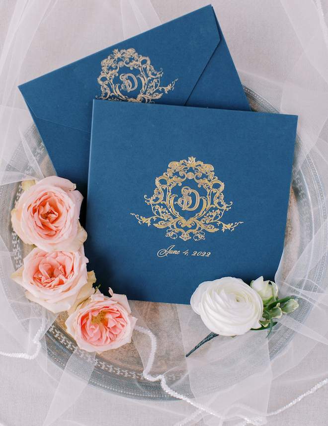 Navy envelopes with a gold monogram and June 4, 2022 written on it. Pink and white roses are next to the envelopes.