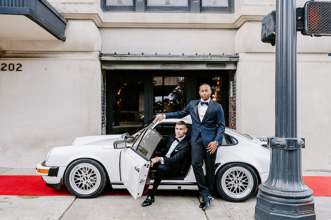 The two grooms pose next to a vintage Porsche outside The Vault at Corinthian Houston. 