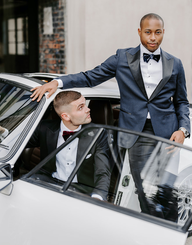 The grooms stand outside of The Vault at Corinthian Houston beside a white vintage Porsche.