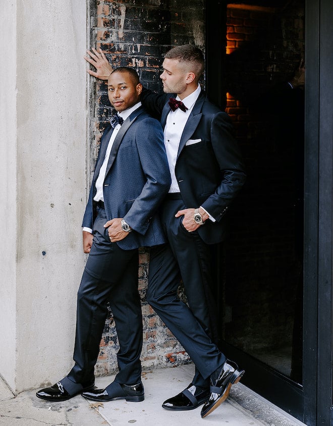 The grooms pose in a door way with exposed brick outside the wedding venue, The Vault at Corinthian Houston.