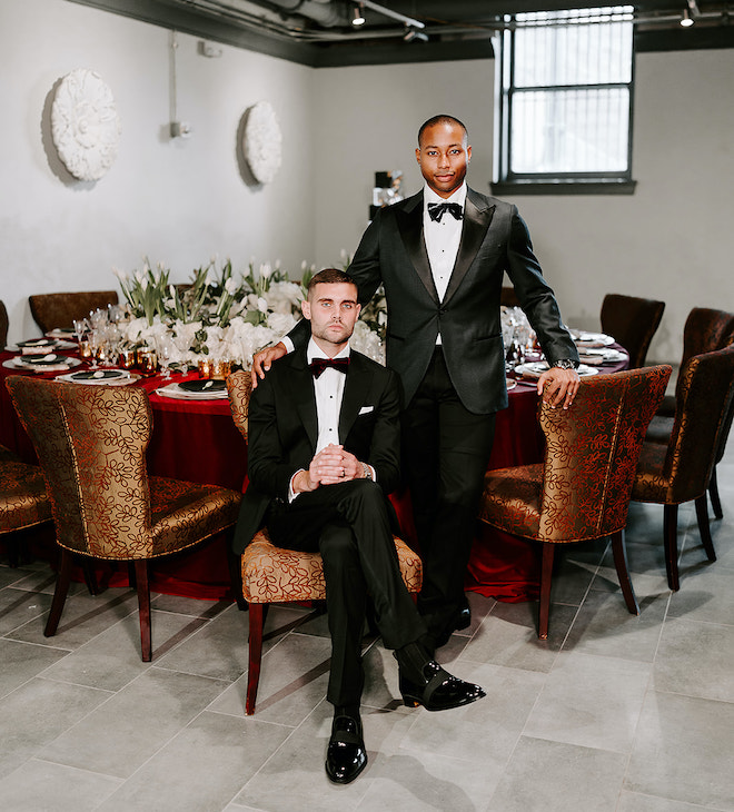 The two grooms pose next to the reception tables at their wedding reception at The Vault Corinthian Houston. 