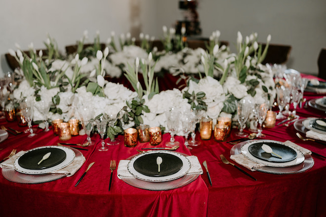 The reception tables are detailed in red linens and warm candlelight surrounded by white roses and greenery. 