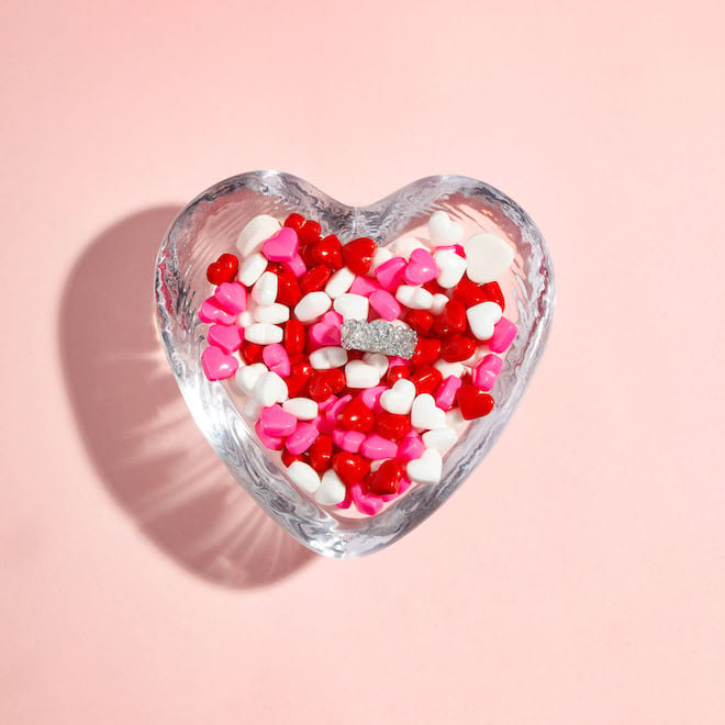 A candy heart dish filled with pink, white and red heart candies and a diamond ring from Zadok Jewelers in Houston, TX