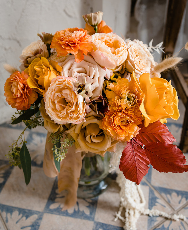 A bouquet of autumnal-colored florals in sand, orange, gold and red.