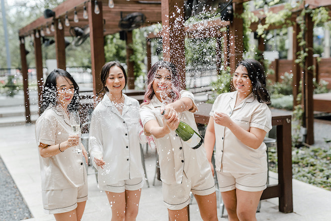 The bridesmaids and bride popping champagne.