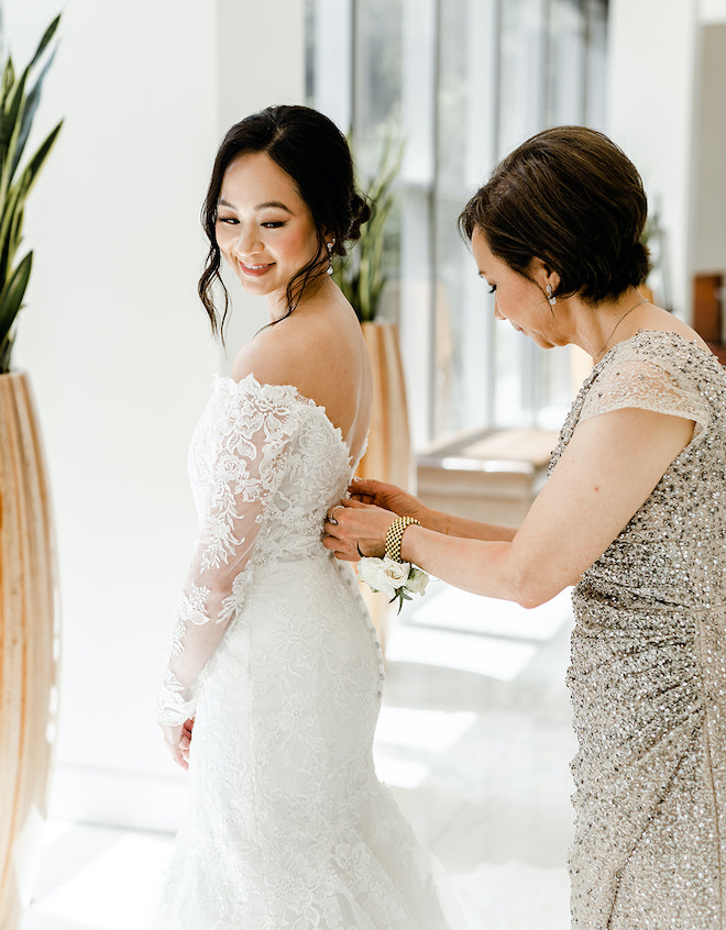 The bride's mother helping the bride button the back of her dress.