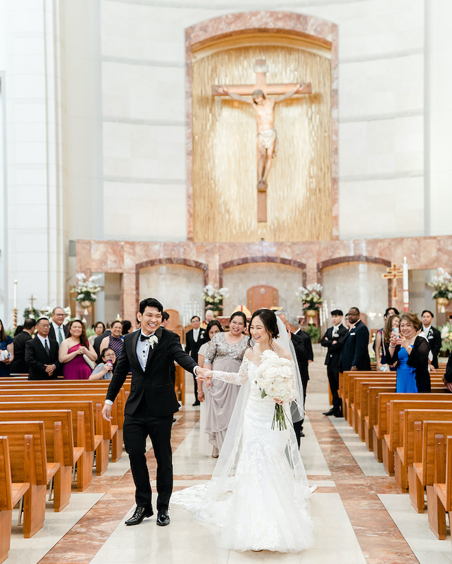 The bride and groom laughing and holding hands as they walk back down the aisle.