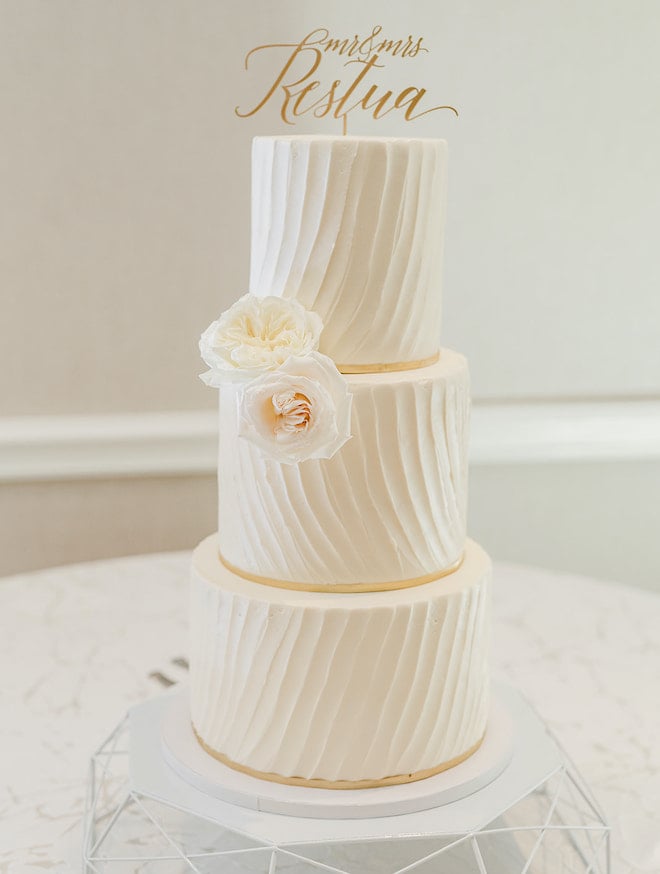 A three tier white and champagne colored wedding cake.