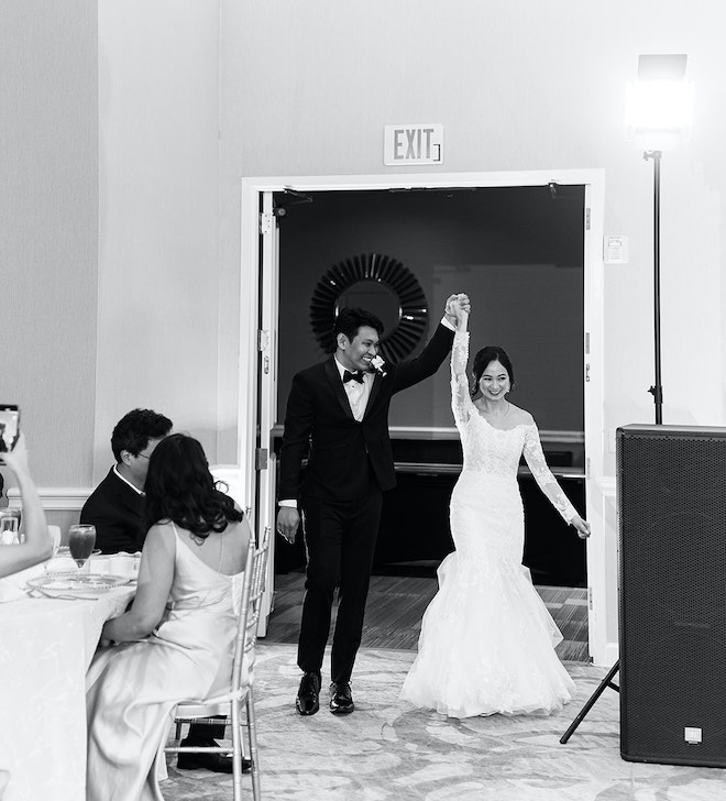 The bride and groom holding their hands in the air as they enter their champagne colored wedding reception.