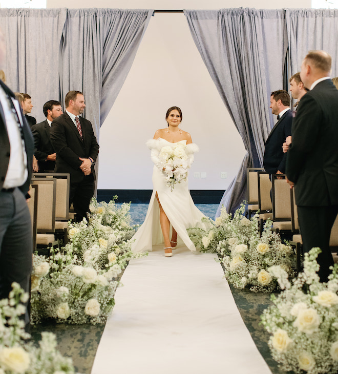 The bride walking down the aisle lined with babys breath and roses.