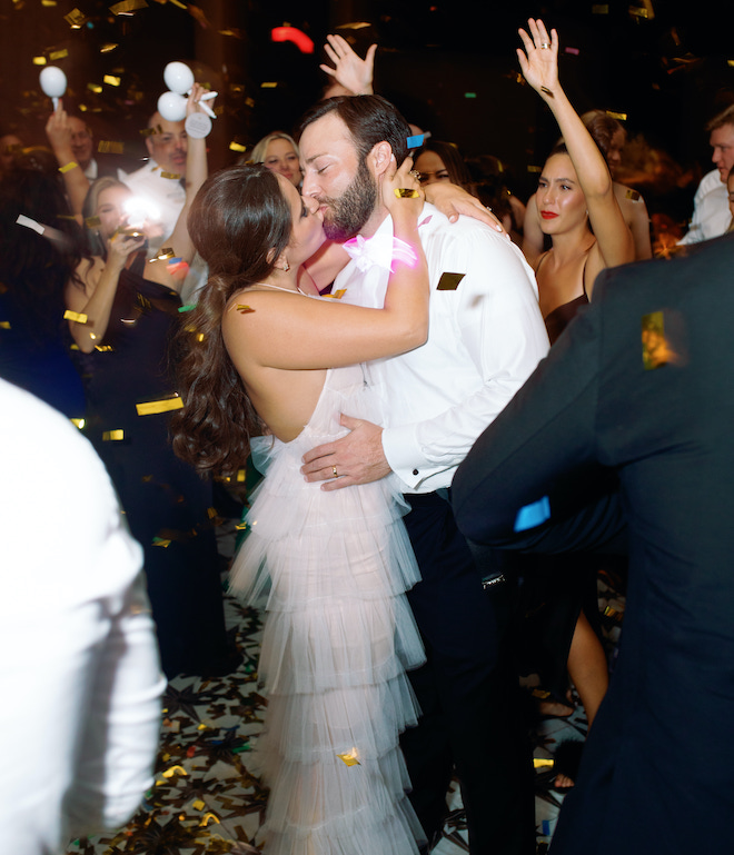 The bride and groom kissing as confetti rains down on them.