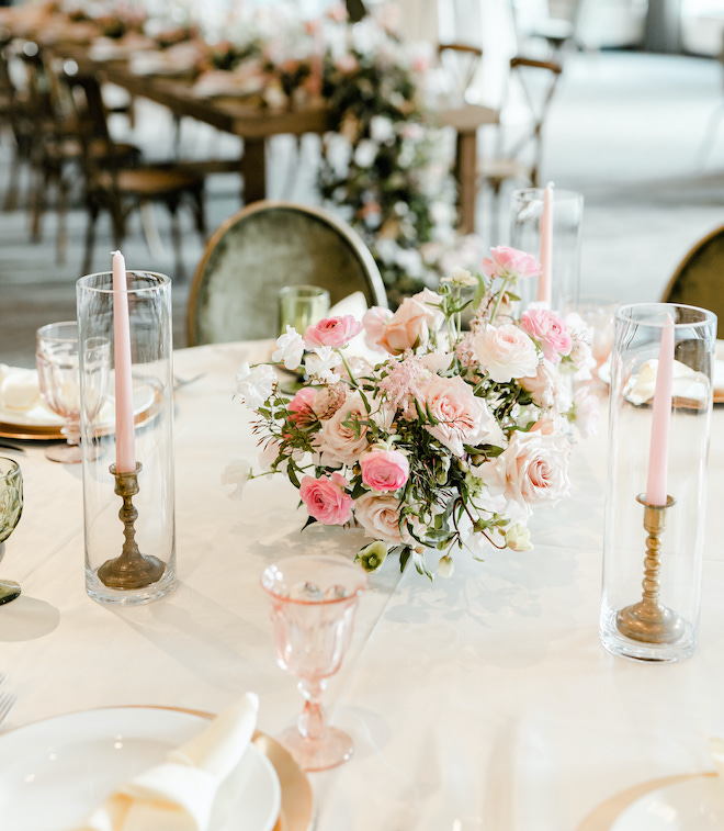 Pink floral centerpiece and pink pillar candles decorating a round table for the light and bright wedding editorial.