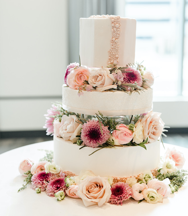A three-tiered wedding cake with florals and peal accents.