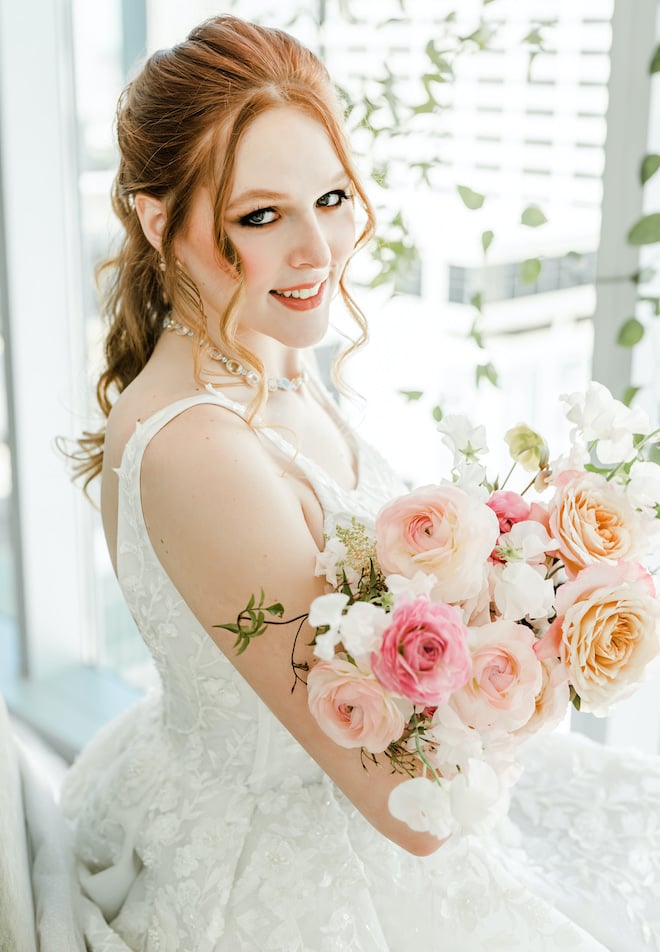 The bride smiling as she holds a bouquet of flowers.