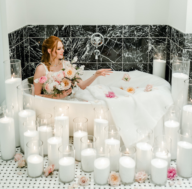 The bride in a bathtub with florals and candlelight.