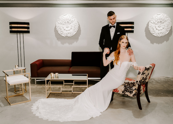 The groom looking down at the bride as she rests on the chair with a soft glam bridal look.