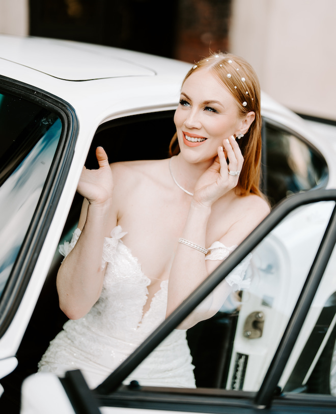 The bride with soft glam makeup, smiling with her hand on her face sitting in a 1987 Porsche 911.