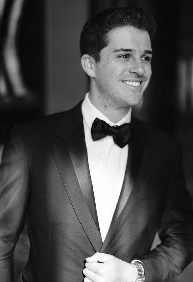 A groom smiling while wearing a tuxedo and bow-tie.