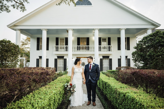 A bride and groom holding hands in front of Ashelynn Manor.