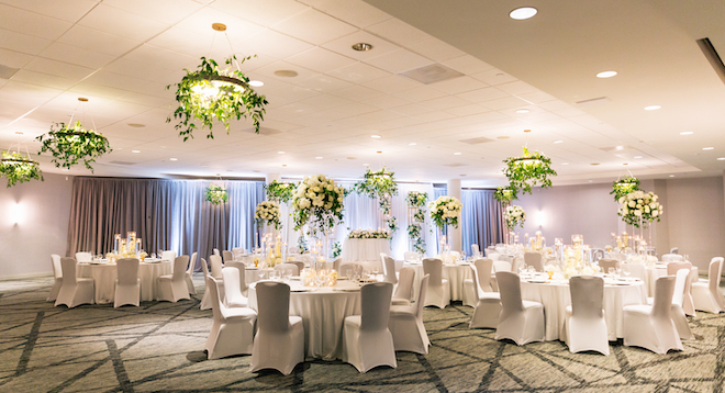 The ballroom at Hyatt Regency Houston decorated with white tables and chairs with greenery on the chandeliers.