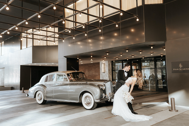 A groom dipping a bride in front of a vintage car at Four Seasons Hotel Houston.