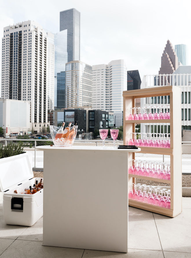 A wine bar set up with pink glasses overlooking the Houston skyline.