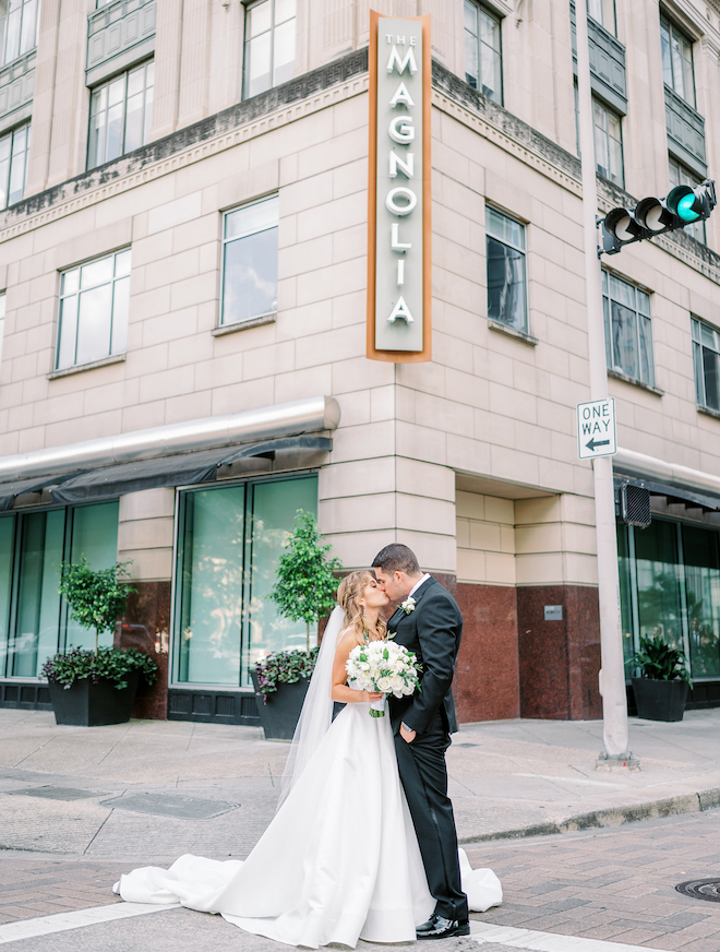 A bride and groom kissing in front of the Magnolia Hotel Houston.
