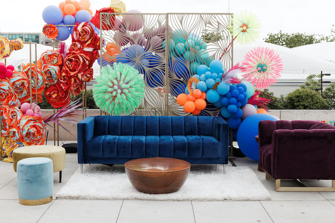 A blue velvet couch with colorful balloons behind it.