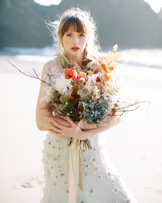 The bride holding a bouquet of orange, blue and white florals on the Oregon Coast.
