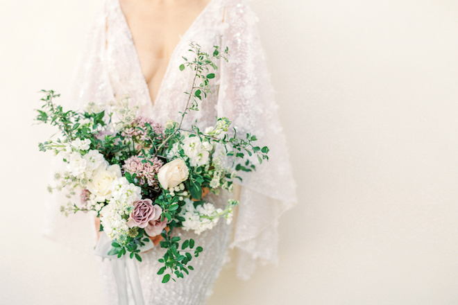 The bride holding a bouquet of greenery, white and mauve florals.