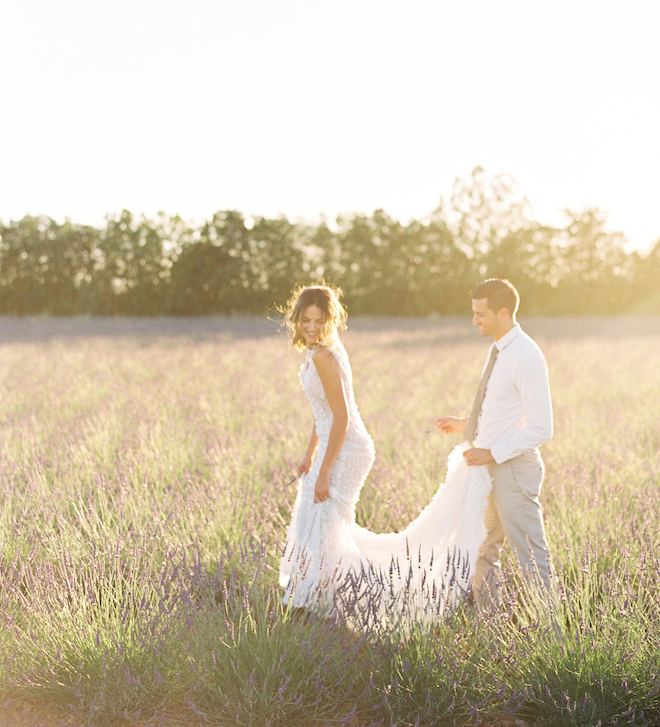 The groom holding the back of the brides gown as they stand in the lavender fields for a romantic elopement editorial in the South of France.