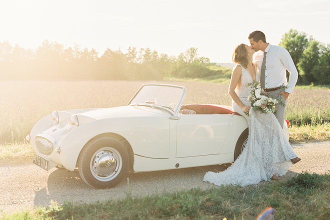 The bride and groom kissing in front of the vintage car in Gordes, France.